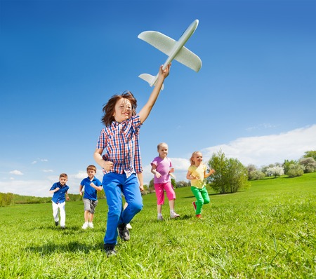 Positive running kids with boy holding big white airplane toy in the field during summer sunny dayの写真素材