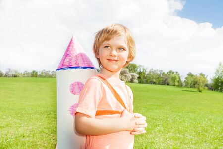 Close-up view of boy with carton rocket toy on his shoulders during sunny day in the green field