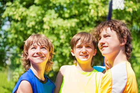 Three happy teenage boys smiling and looking together up outside during summer sunny dayの写真素材