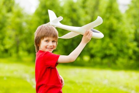 Smiling boy holding white airplane toy in the green meadow during summer sunny dayの写真素材