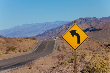 Road with curved arrow yellow sign in desert, California, United States