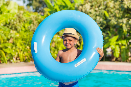 Boy in hat who holds inflatable ring standing near the swimming pool outside in summerの写真素材