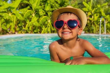 Boy in heart-shaped sunglasses on green airbed in the swimming pool outside in summerの写真素材
