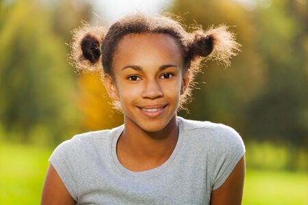Portrait of beautiful African girl sitting on green grass in park during sunny autumn dayの写真素材