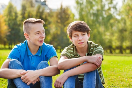 Two teens sitting together on green meadow during wonderful sunny autumn dayの写真素材