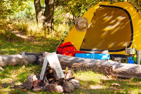 Campsite with tent, backpack and bonfire during beautiful sunny day in the forestの写真素材