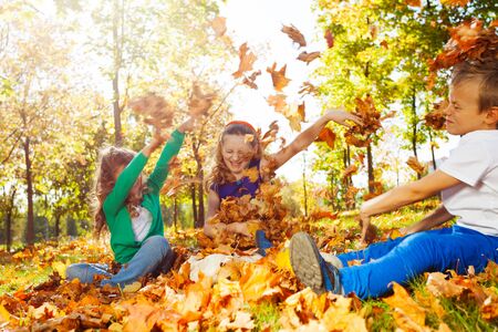 Happy friends having fun with thrown leaves in the forest together during beautiful autumn sunny dayの写真素材