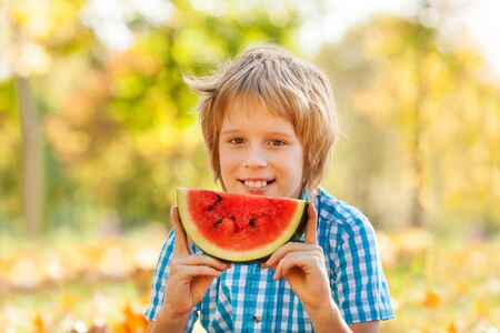 Happy boy holding watermelon sitting on the leaves in forest during autumn dayの写真素材