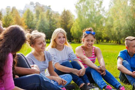 Happy international friends sitting together on green meadow during wonderful sunny autumn dayの写真素材