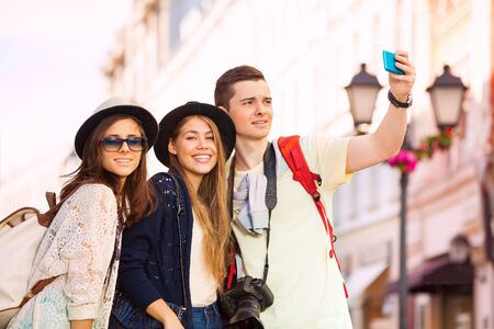 Three friends taking selfie with mobile phone during sightseeing on the European street during summer day timeの写真素材