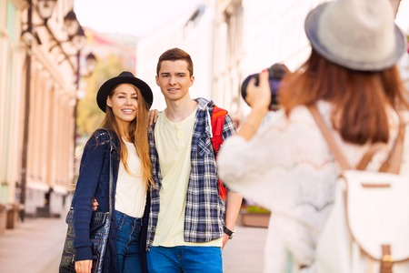 Boy and girl smiling standing close and girl shooting them with professional camera on the European street during summer day timeの写真素材