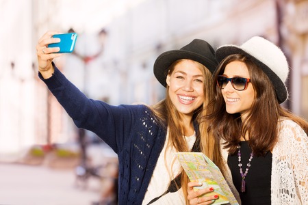 Two cute girls taking selfies with mobile phone during sightseeing on the European street during summer day timeの写真素材