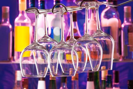 Night bar with bottles and color lit background and wine glasses hang upside downの写真素材