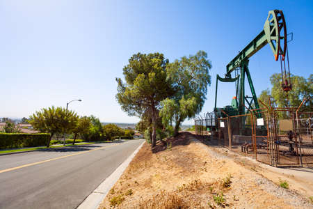 One green oil-derrick fencing by chain-link  to the right of the road against the blue sky