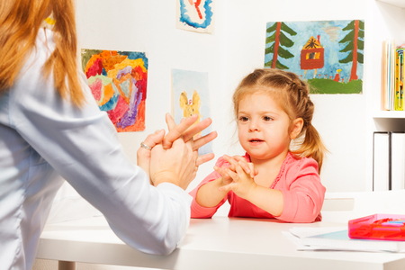 One little preschooler playing finger games with her teacher at the tableの写真素材
