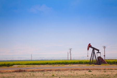 One big steel oil-derrick operating between green field and road at the sunny dayの写真素材