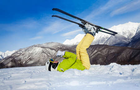 Woman with mountain ski outfit laying in snow in moving pose upside down making fun of skiingの写真素材