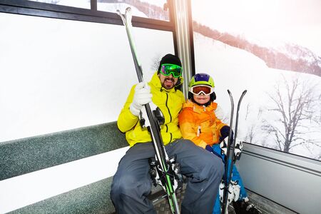 Dad and son sit in cable car and holding ski lifting upの写真素材