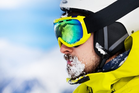 Close portrait of a man with beard and ski mask and helmet with snow on beardの写真素材