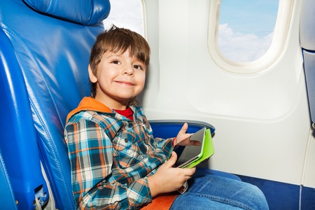 Little boy sit with tablet computer in the airplane flying commercial linerの写真素材