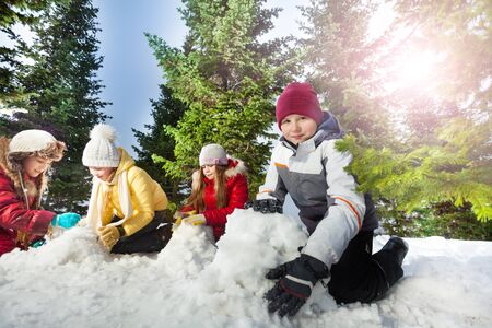Four kids, boy and girls making snowman at beautiful forest, funny winter occupationの写真素材