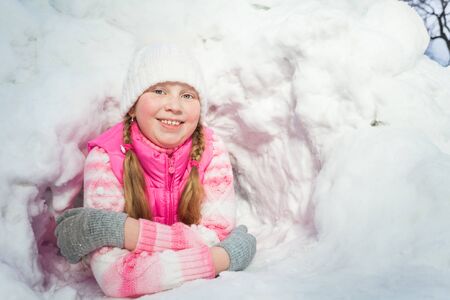 Smiling girl in pink clothes laying at the snow holeの写真素材