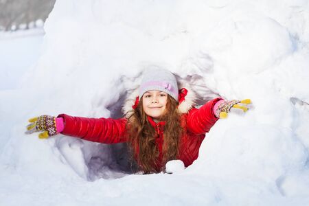 Amusing smiling girl in the winter playing at a snow cave