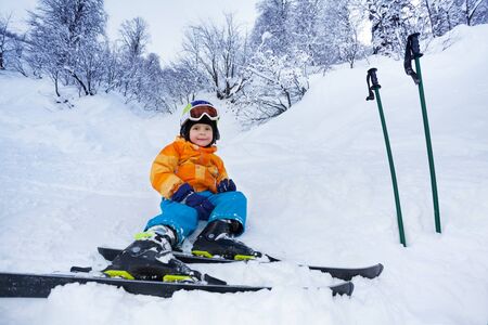 Little skier boy sit in snow resting after ski school lessonの写真素材
