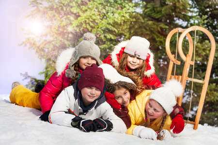 Happy friends one boy and four girls laying at the snow in winter forestの写真素材