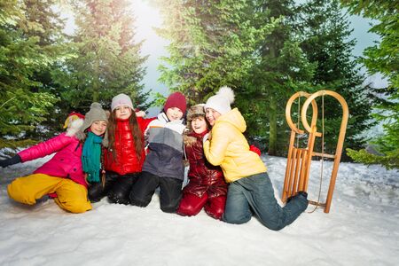 Row of group of kids boys and girls standing together on their knees outside in snowy forestの写真素材