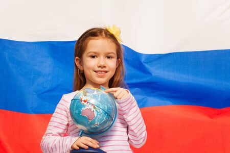 Beautiful schoolgirl pointing to the globe by her finger standing against flag of Russian Federationの写真素材