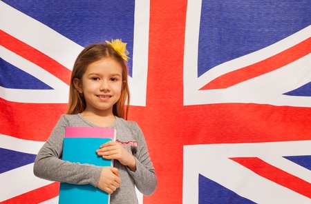 Smiling English schoolgirl standing with  textbooks, flag of Great Britain at the backgroundの写真素材