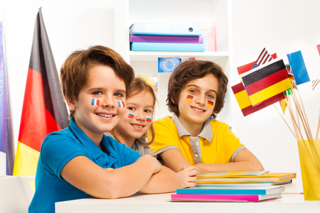 Three happy children  with flags on cheeks sitting at the classroom and studying geographyの写真素材