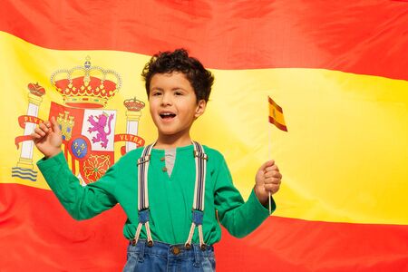 Happy Hispanic boy with flag in his hand against big waving Spanish flagの写真素材