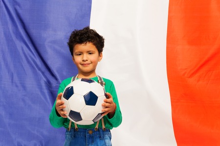 Little football fan, boy holding his ball against French flagの写真素材