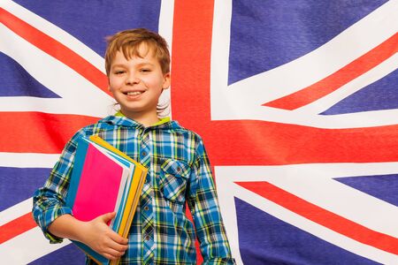 Smiling schoolboy with textbooks in his hand standing against English flagの写真素材