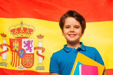 Smiling schoolboy with his textbooks standing against the flag of Spainの写真素材