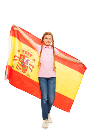 Beautiful young girl with two long plaits holding unfolded Spanish flag behind her back, isolated on whiteの写真素材