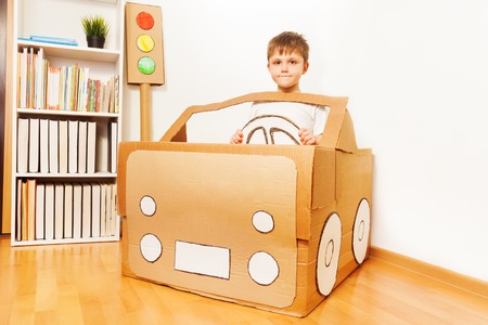 Creative kid boy plays with his handmade cardboard car at homeの写真素材