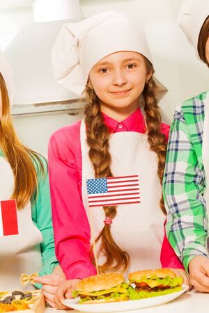 Beautiful young cook, girl in apron and cook hat with American flag and hamburgers on the plateの写真素材