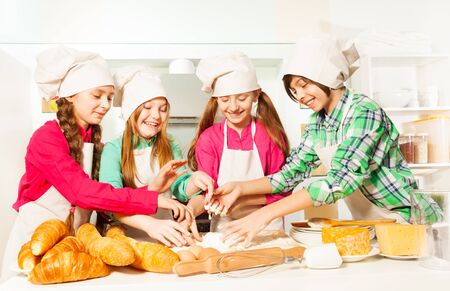 Four kids, young bakers in cook's uniform, kneading dough with flour and eggs in the kitchenの写真素材