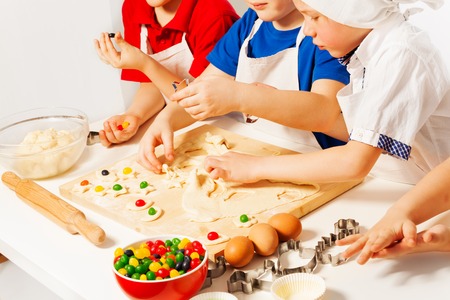 Kids in white aprons making candy filled cookies with cookie cutters on wooden deskの写真素材