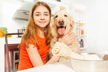 Portrait of happy teenage girl with her Golden Retriever doggy sitting in the kitchen