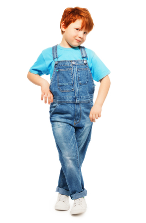 Full-length photo of cute redheaded five years old boy in overall and blue t-shirt, isolated on whiteの写真素材