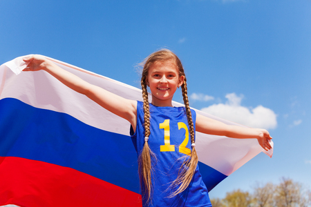 Portrait of beautiful teenage girl in sportswear, standing with Russian flag behind her, outdoor on sunny dayの写真素材