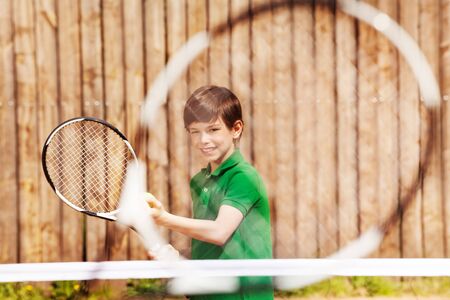 Happy young tennis player, kid boy holding racket and ball, preparing to serve, view through the racket netの写真素材