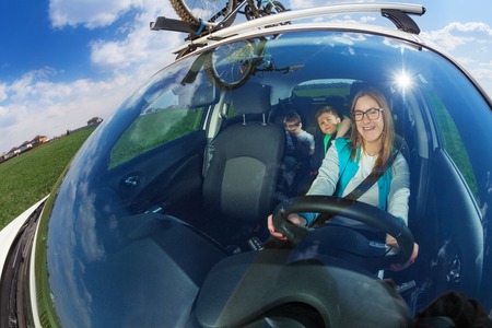 Happy female driver travelling by car with two kid boys on sunny day, view through a windscreen,...