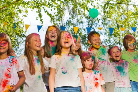 Happy age-diverse kids painted in colors of Holi festival, standing in a row outsideの写真素材