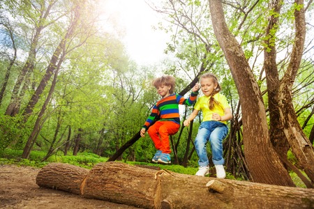 Portrait of two happy five years old kids, jumping over a log in the summer forestの写真素材