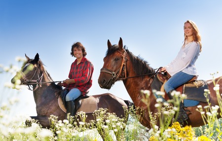 Side view portrait of smiling young couple horseback riding on purebred horses in flowery meadowsの写真素材